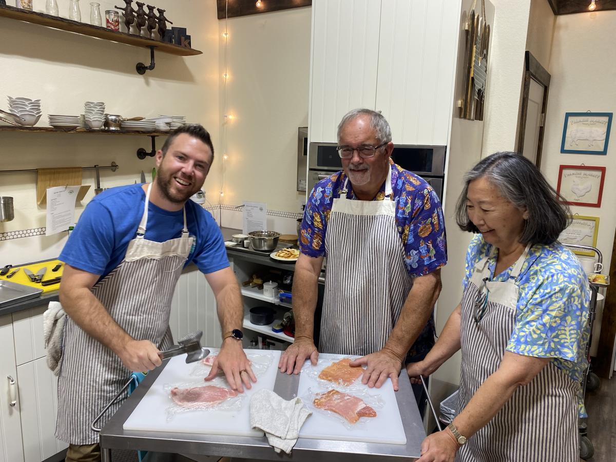 Four people pounding chicken breasts