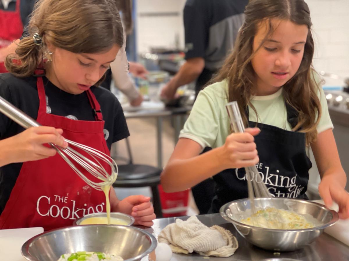 Two kids whisking a mixture in metal bowls at a cooking class