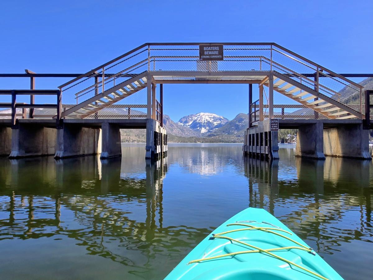 Kayak in the channel entering Grand Lake under a walking bridge with Mount Baldy in the background