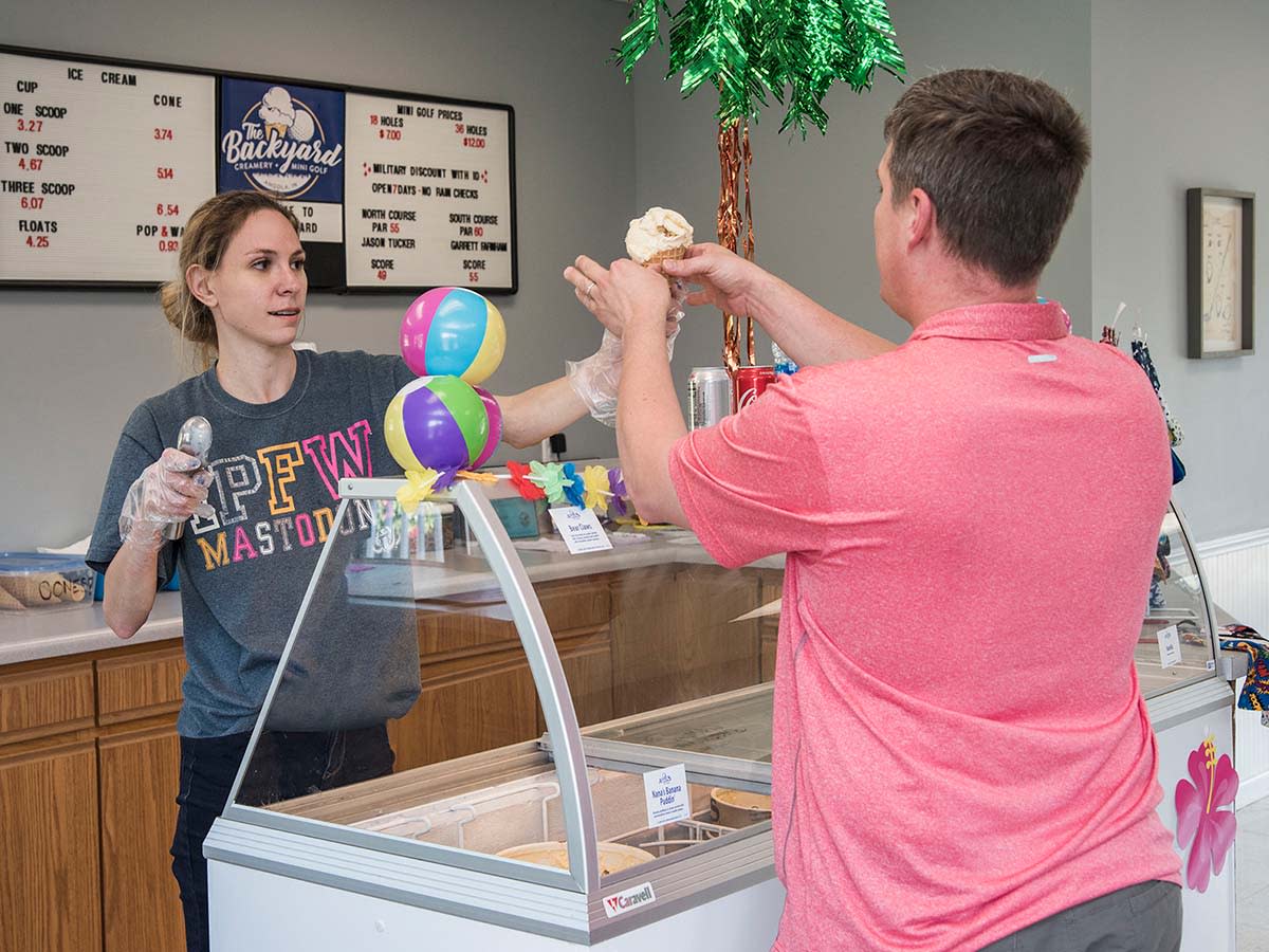A store employee handing an ice cream cone to a nab across a counter at The Backyard Creamery & Mini Golf in Steuben County.