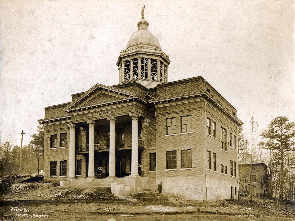 Sepia photo of the newly built Jackson County Courthouse in Sylva, NC, around 1914, with its columned portico and domed cupola on a bare dirt hillside