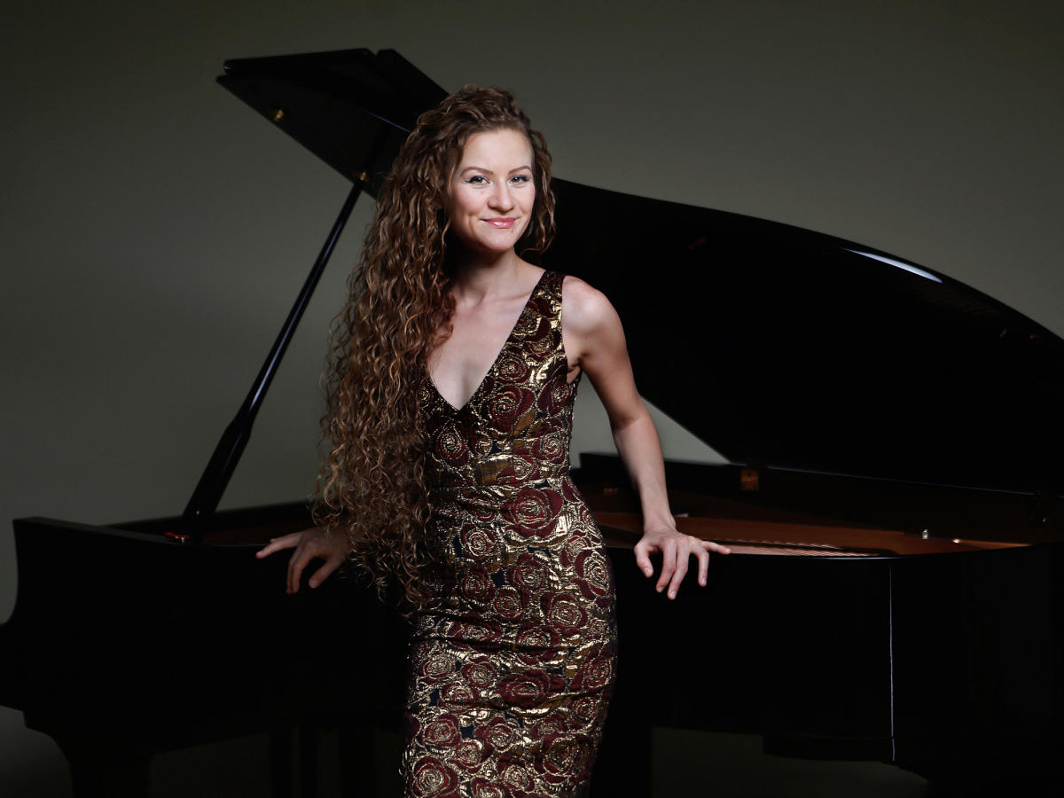 Asiya Korepanova posing at the piano in a gold rose dress.