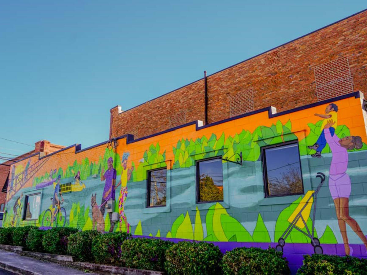 A mural depicting hiking and biking on the side of the Downtown Clayton, NC Moveology building.