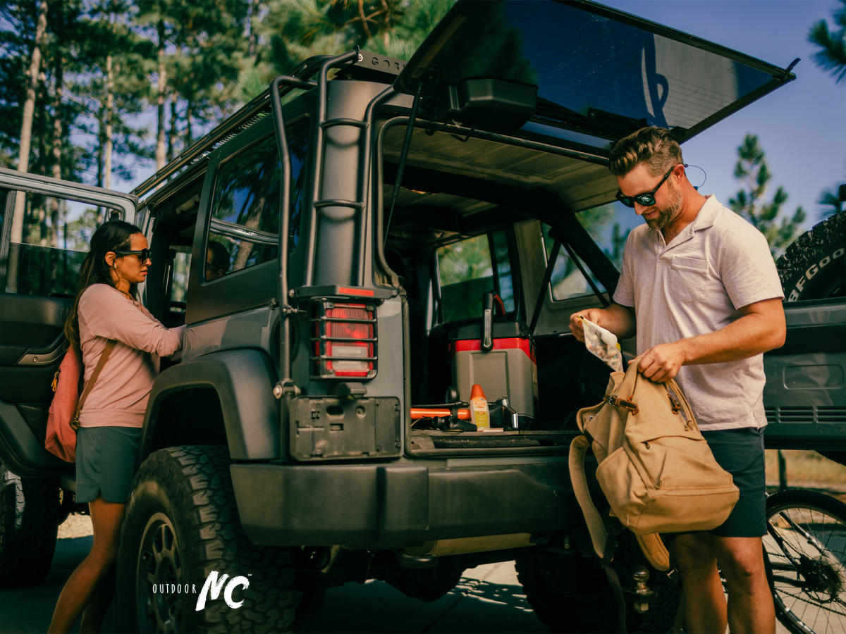 A couple getting ready to go biking, packing their packs from the back of their SUV.