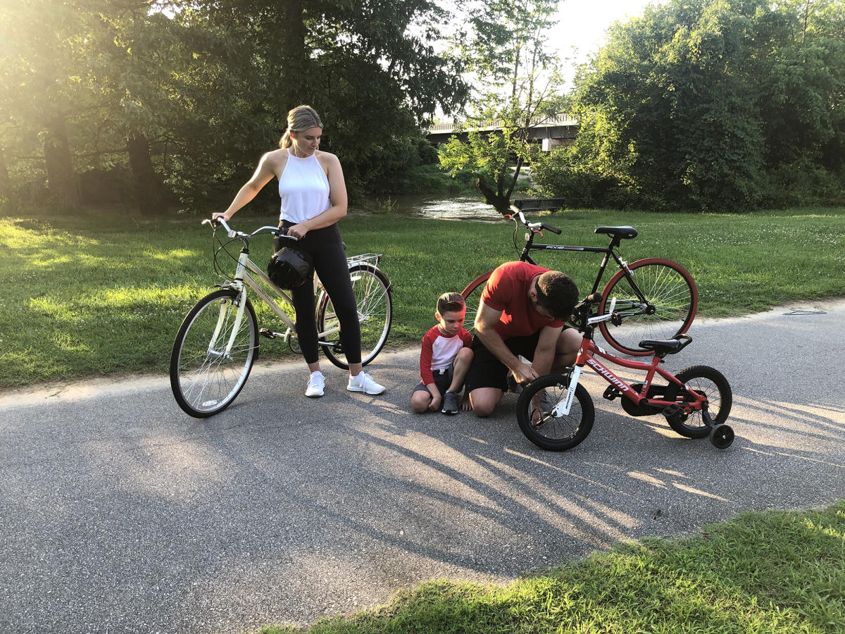 A father helps his son fix his bike while the mom looks on