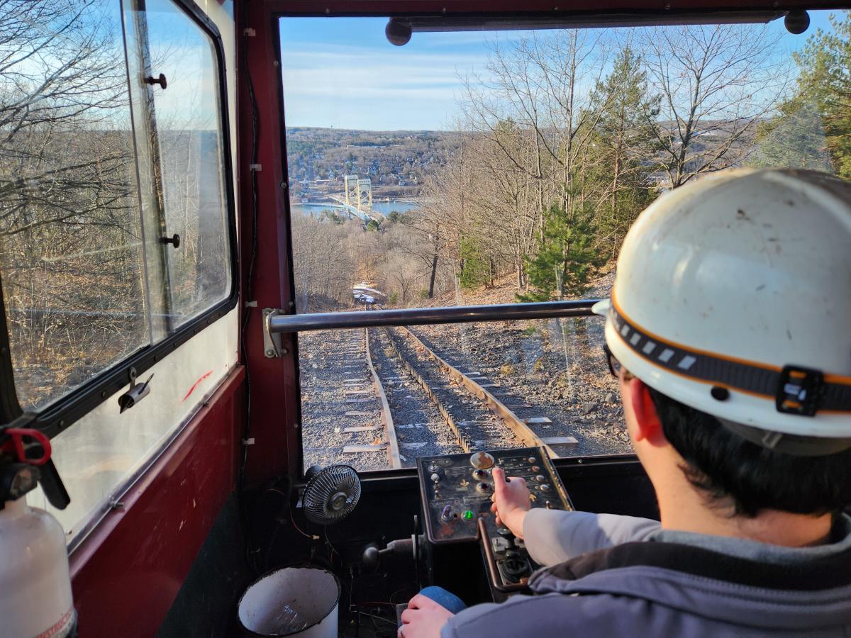 uphill view of a bridge and river from inside a rail tram over a person's shoulder