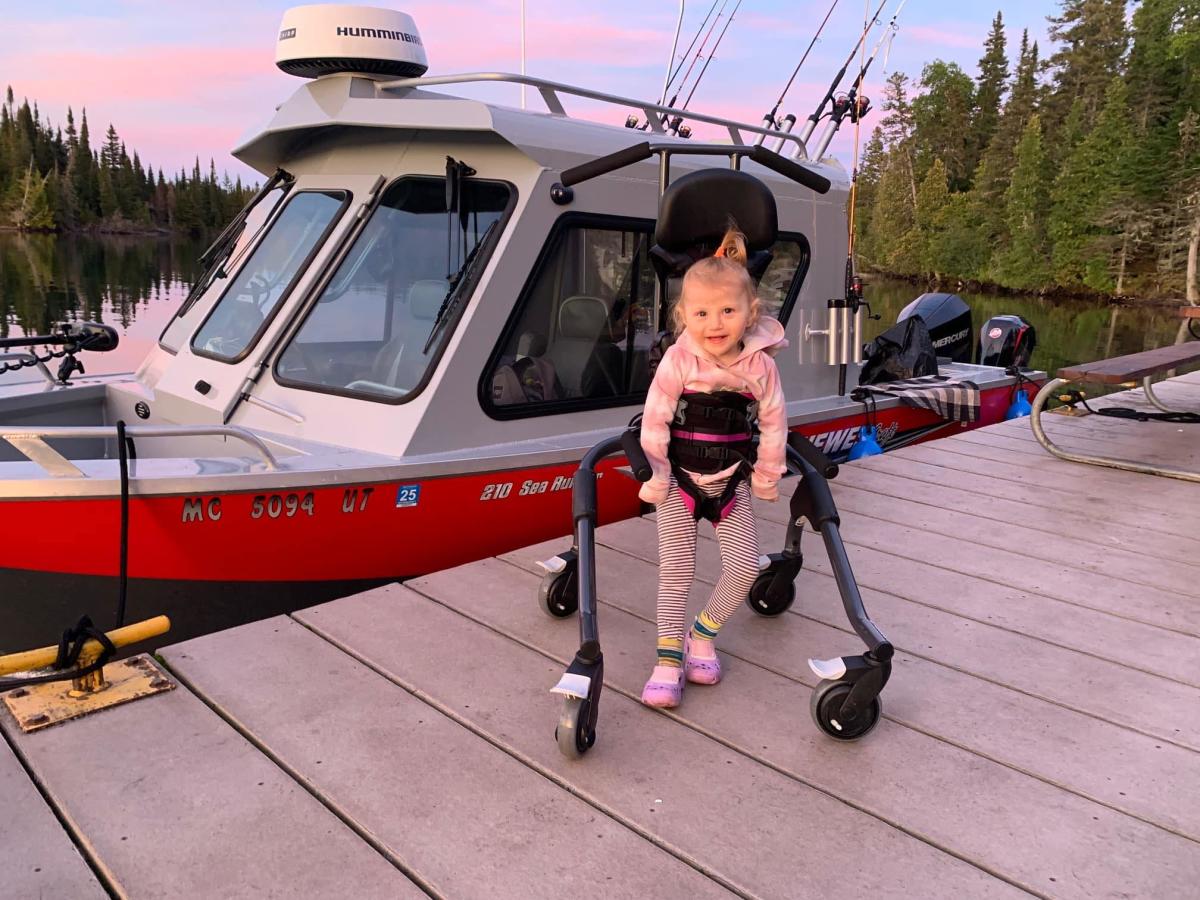 Young child stands in front of boat using a walker.