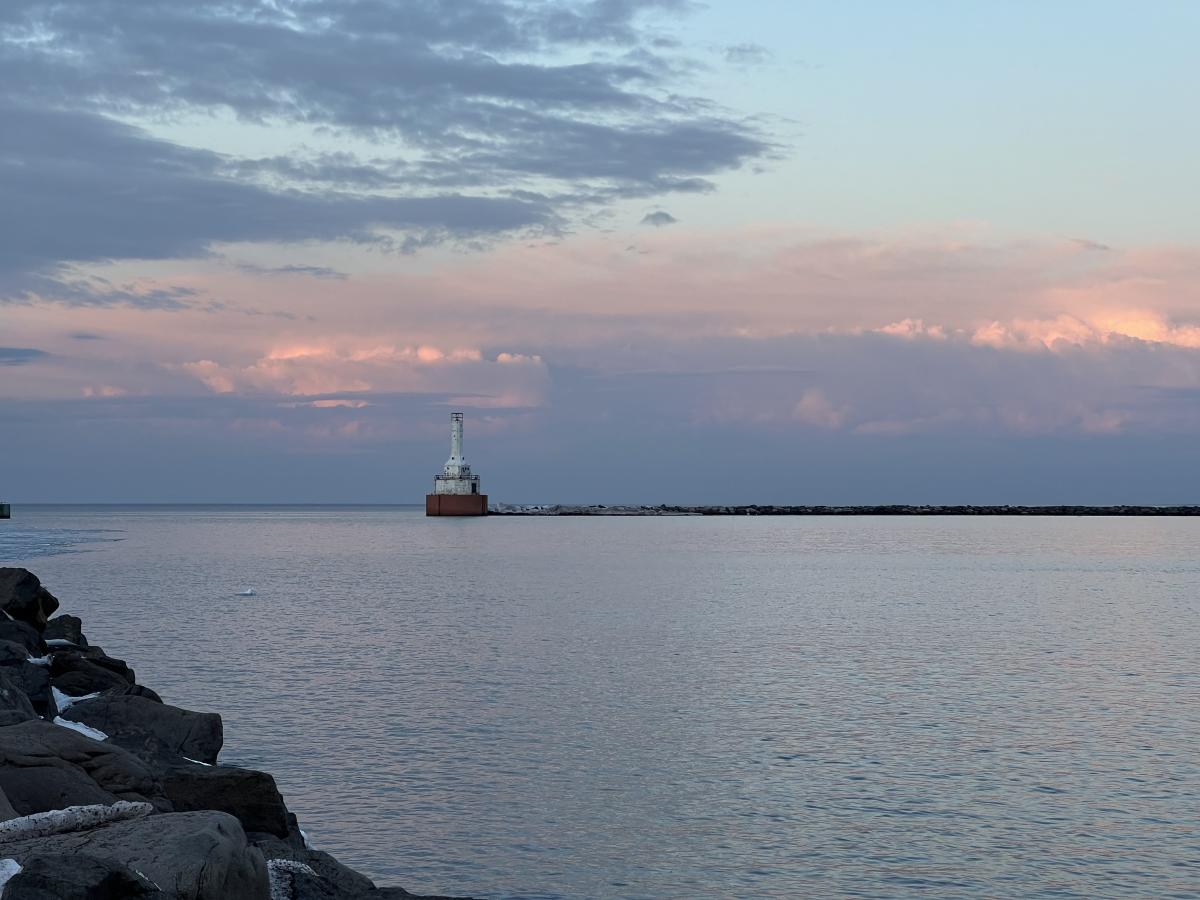 a sunset sky over the lake, a lighthouse in the distance