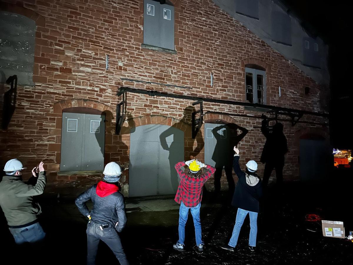 people in hardhats play with shadows against a brick building