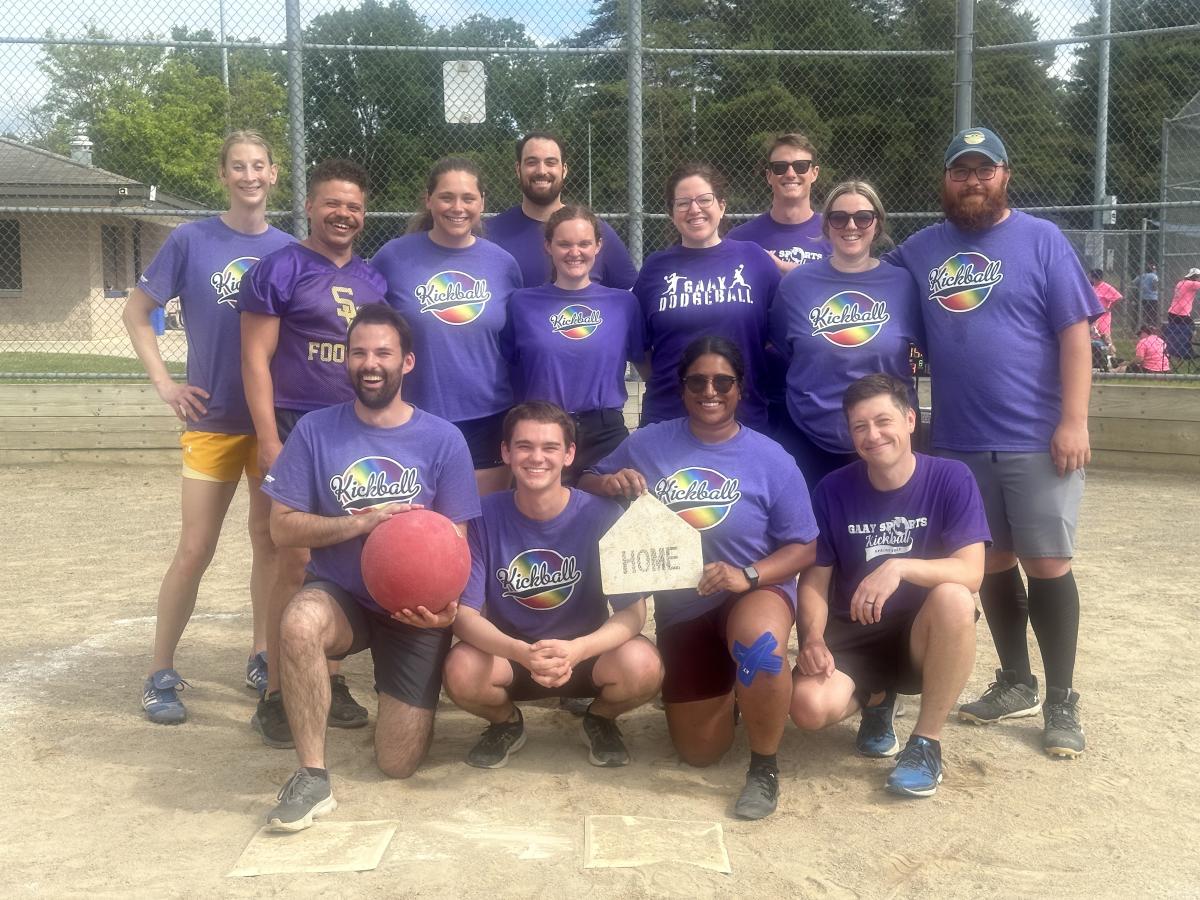 A group of athletes in purple T-shirts posing with a dodgeball and a trophy and smiling at the camera.