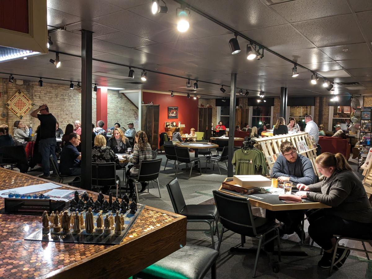 Interior of a game lounge with groups of people playing board games at tables.