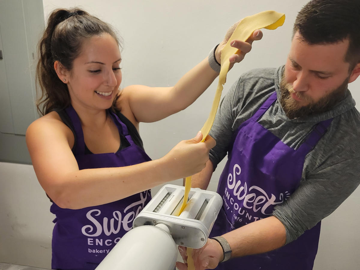 A man and a woman wearing purple aprons pressing dough.