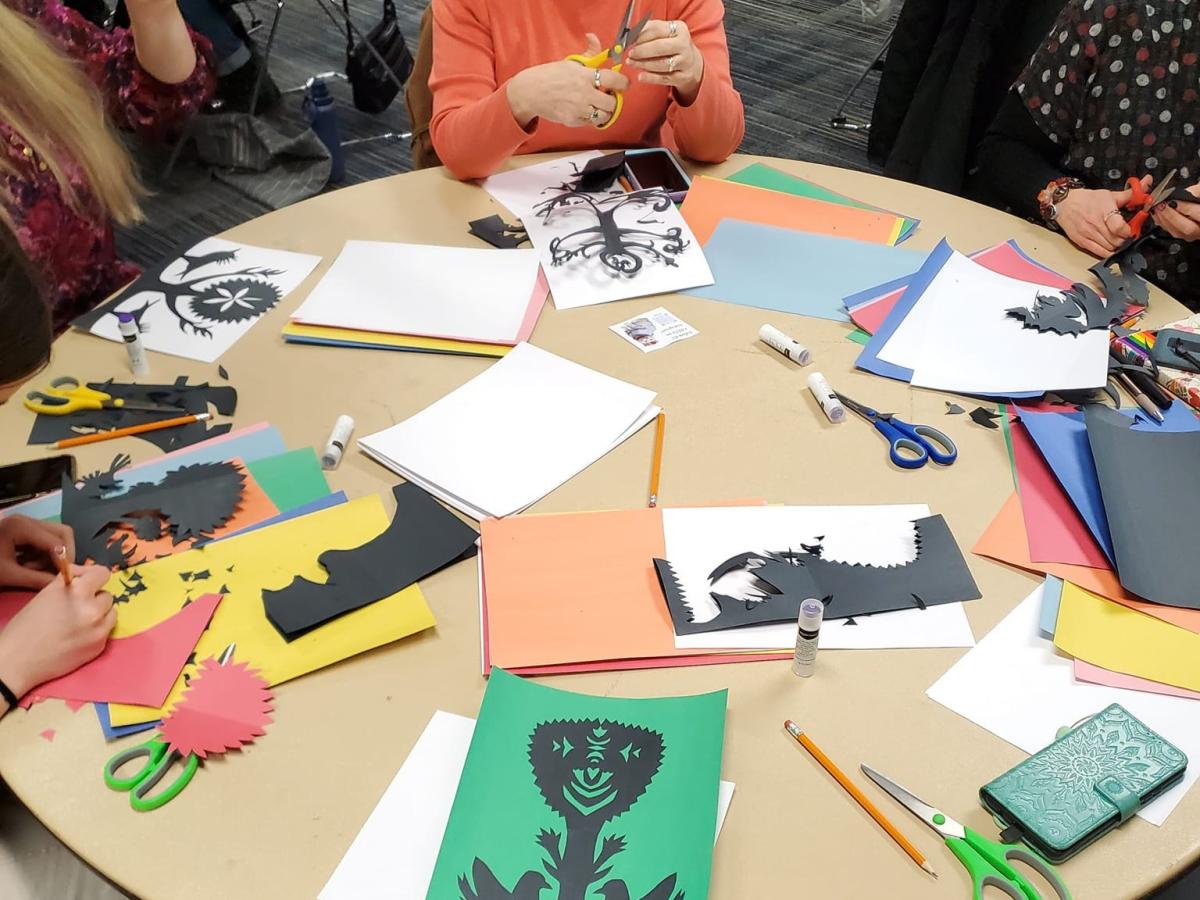 Photo of a round table with people sat around, cutting paper to create Polish wycianki.