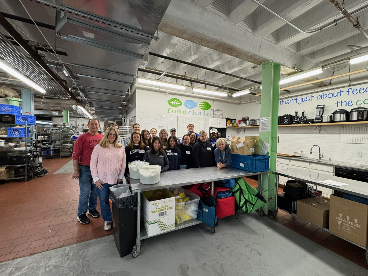 A group of people stand behind a stainless steel counter top in an industrial kitchen.