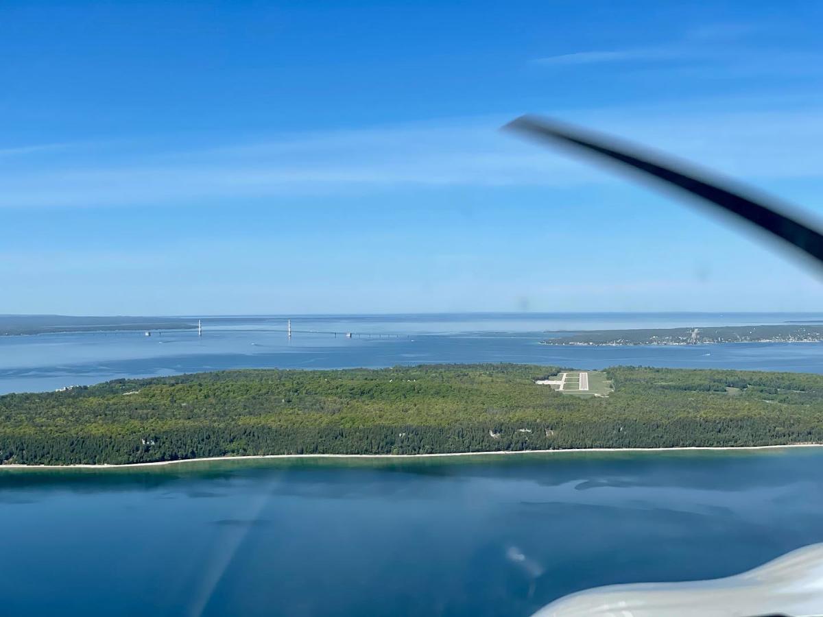 Mackinac Island Airport runway seen from a plane above with Mackinac Bridge on the horizon