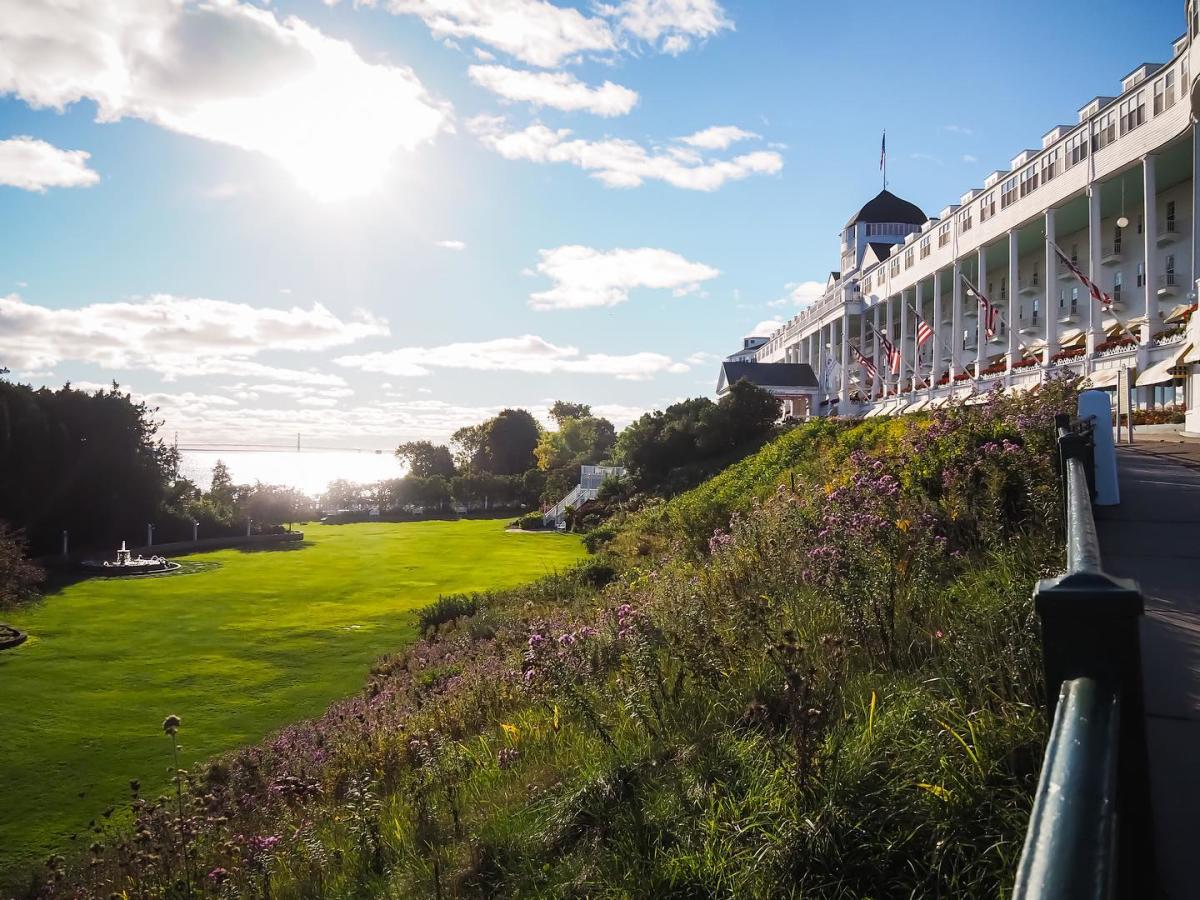 Sun shimmers on the horizon above the Mackinac Bridge with Mackinac Island’s Grand Hotel in foreground