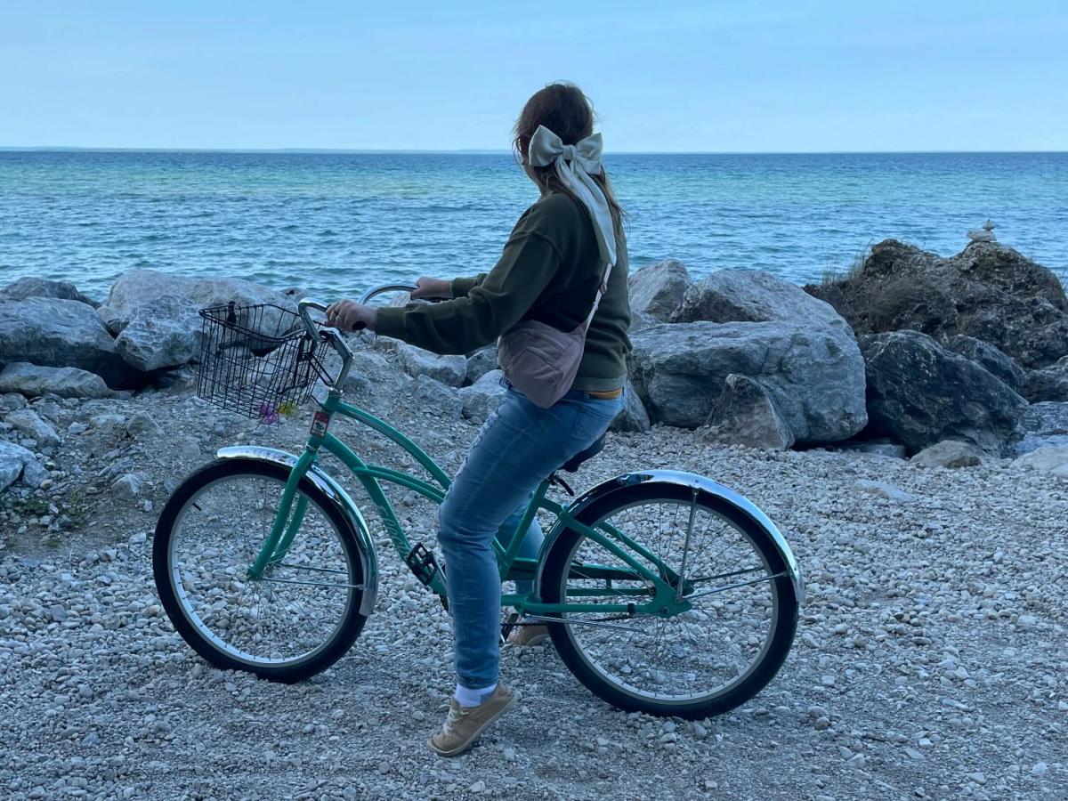 Young woman sits on a parked bicycle looking out over the water around Mackinac Island