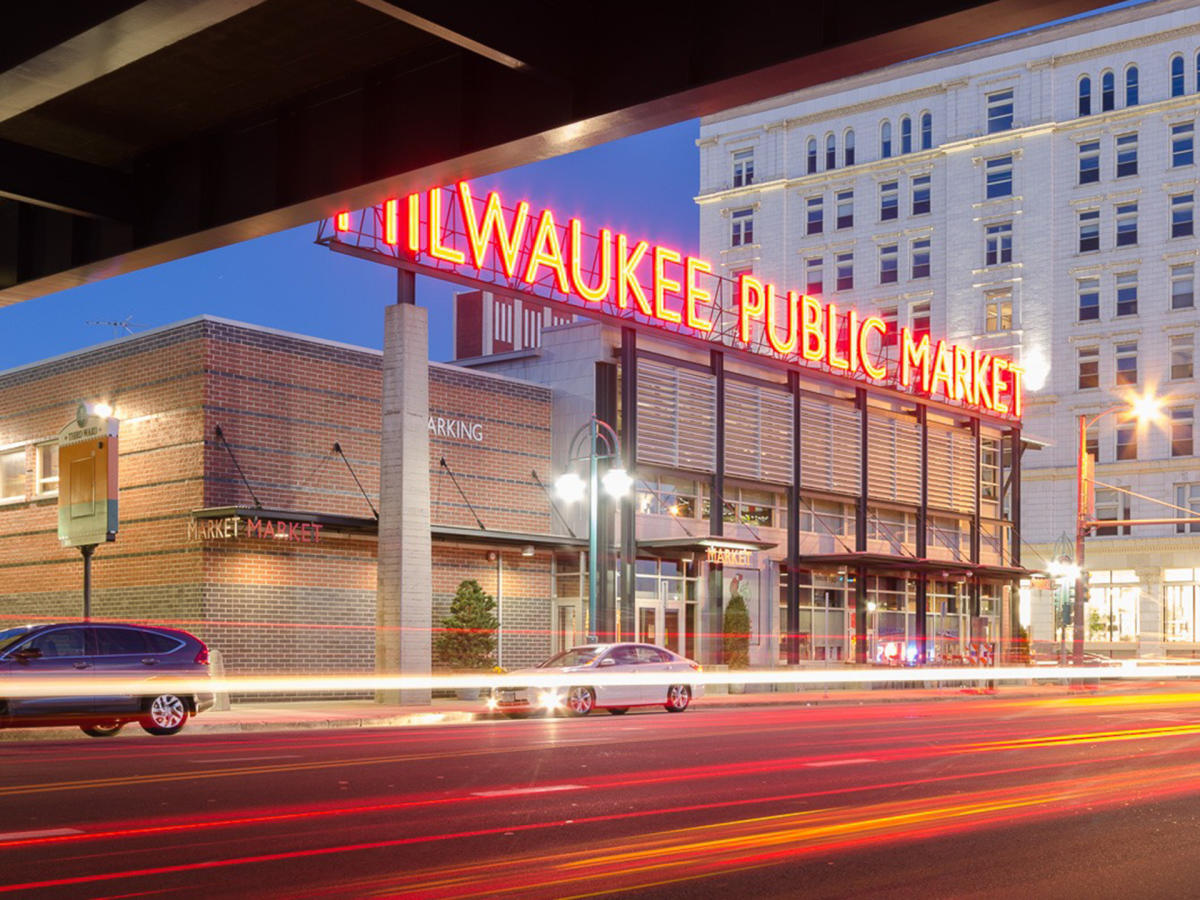 An exterior shot of the Milwaukee Public Market at dusk with the lights of the sign showing bright red against the sky