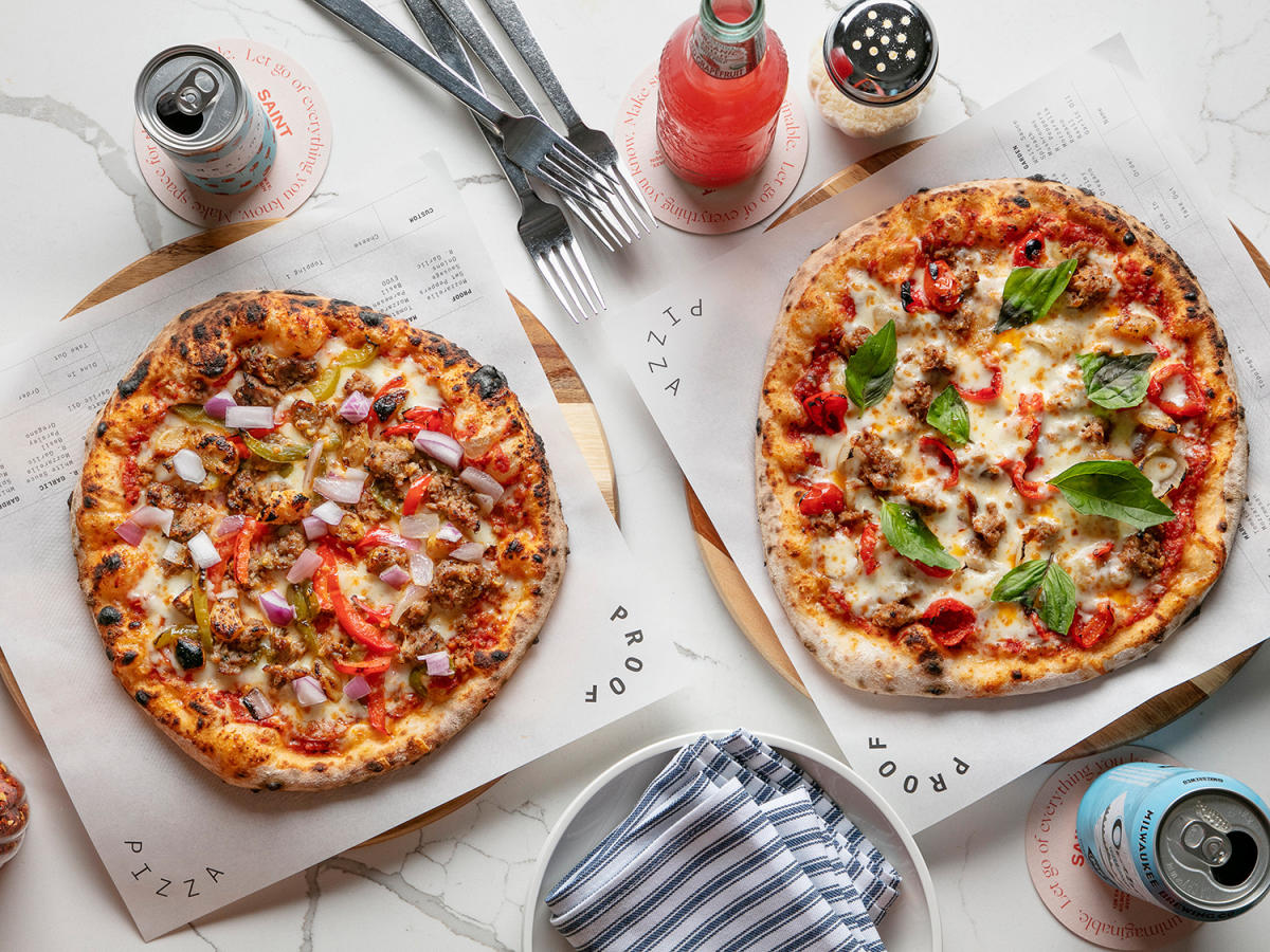 a photo of two pizzas on a marble table with fixings, drinks and silverware