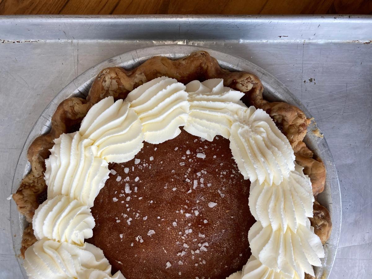 Whole pie with a golden brown filling topped with piped whipped cream and coarse sugar crystals in a flaky crust on a metal tray.