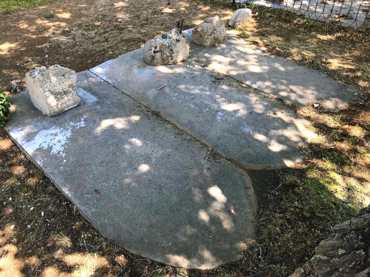 Weathered concrete grave coverings and small stone markers lie beneath dappled tree shade.