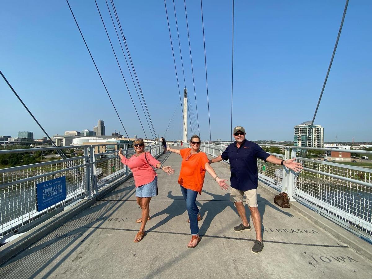 Three people standing with one foot in Nebraska and one foot in Iowa (called Bobbing) on the Bob Kerrey Pedestrian Bridge.