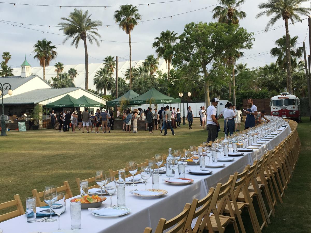 A long dinner table covered in a white tablecloth in the Rose Garden VIP area, part of Outstanding in the Field at Coachella Valley Music & Arts Festival