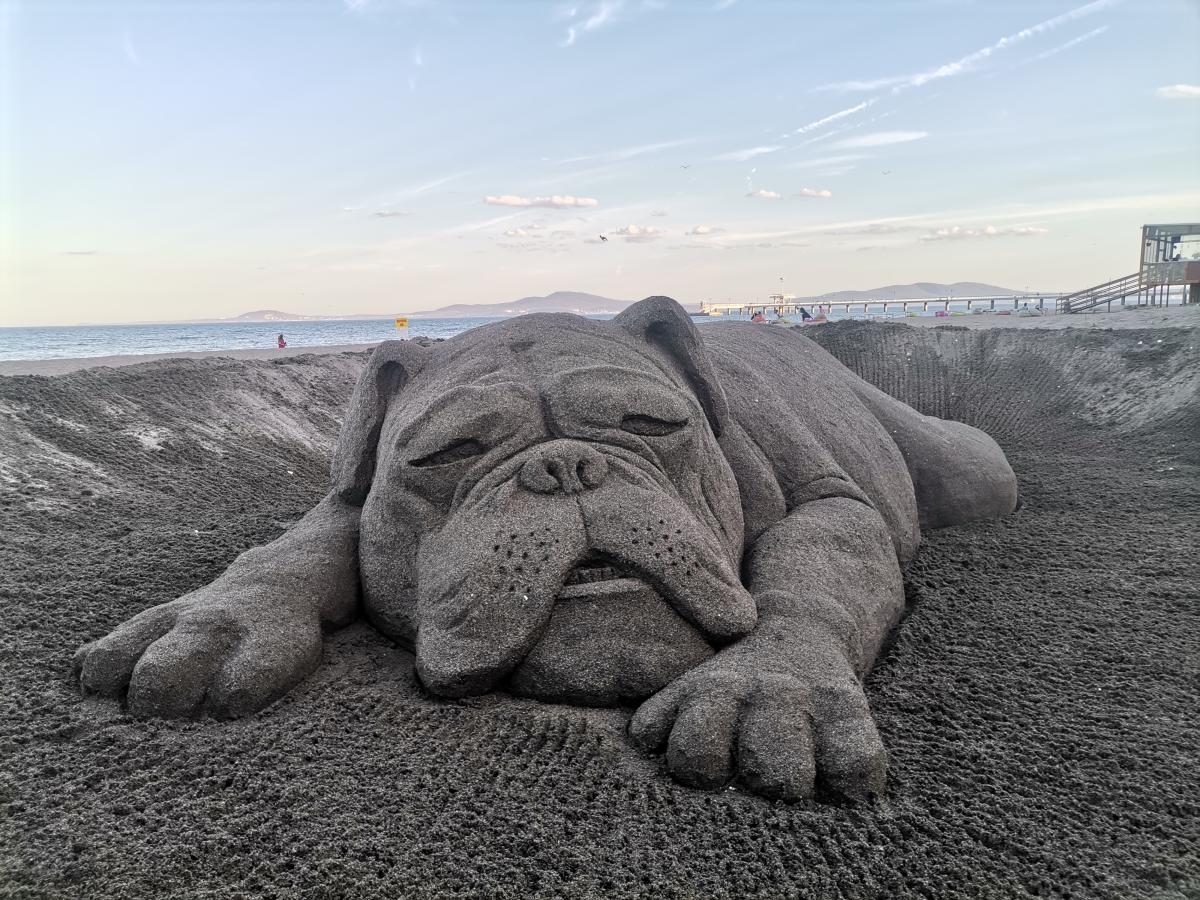 Sand sculpture of a dog laying out on its tummy