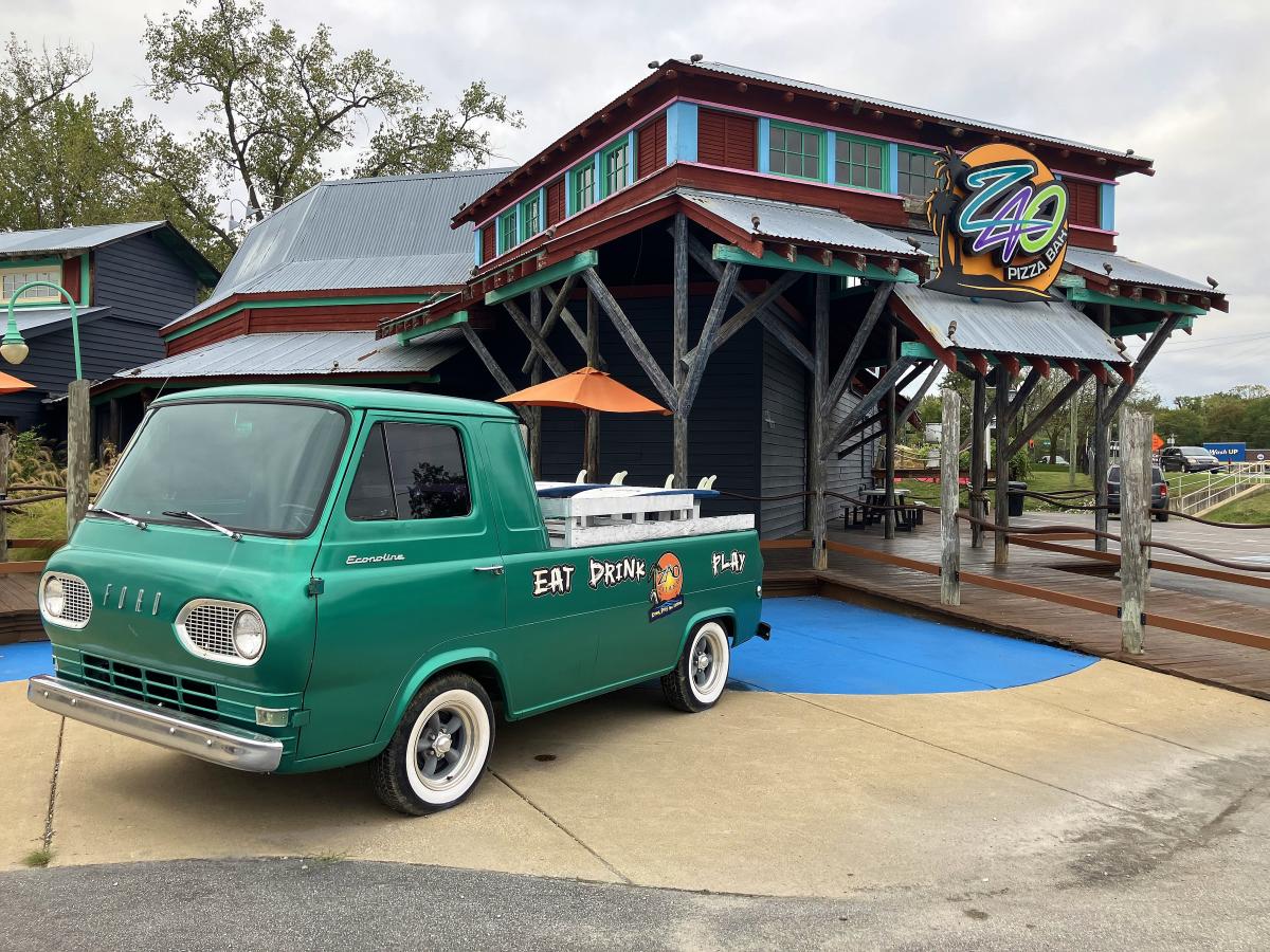A green vintage pickup truck sits outside of a family fun center.
