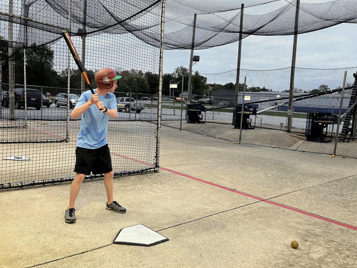 A teen boy in a blue tshirt and black shorts holds a bat waiting to hit a baseball.