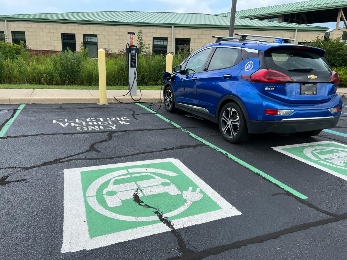 A blue car is charging at an electric station in a parking lot.