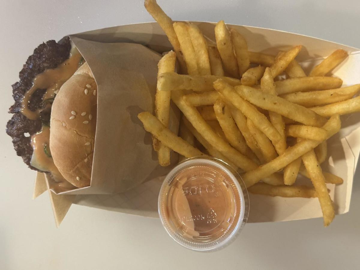 A closeup shot of a smashburger wrapped in brown paper with crip fries next to it in a basket.