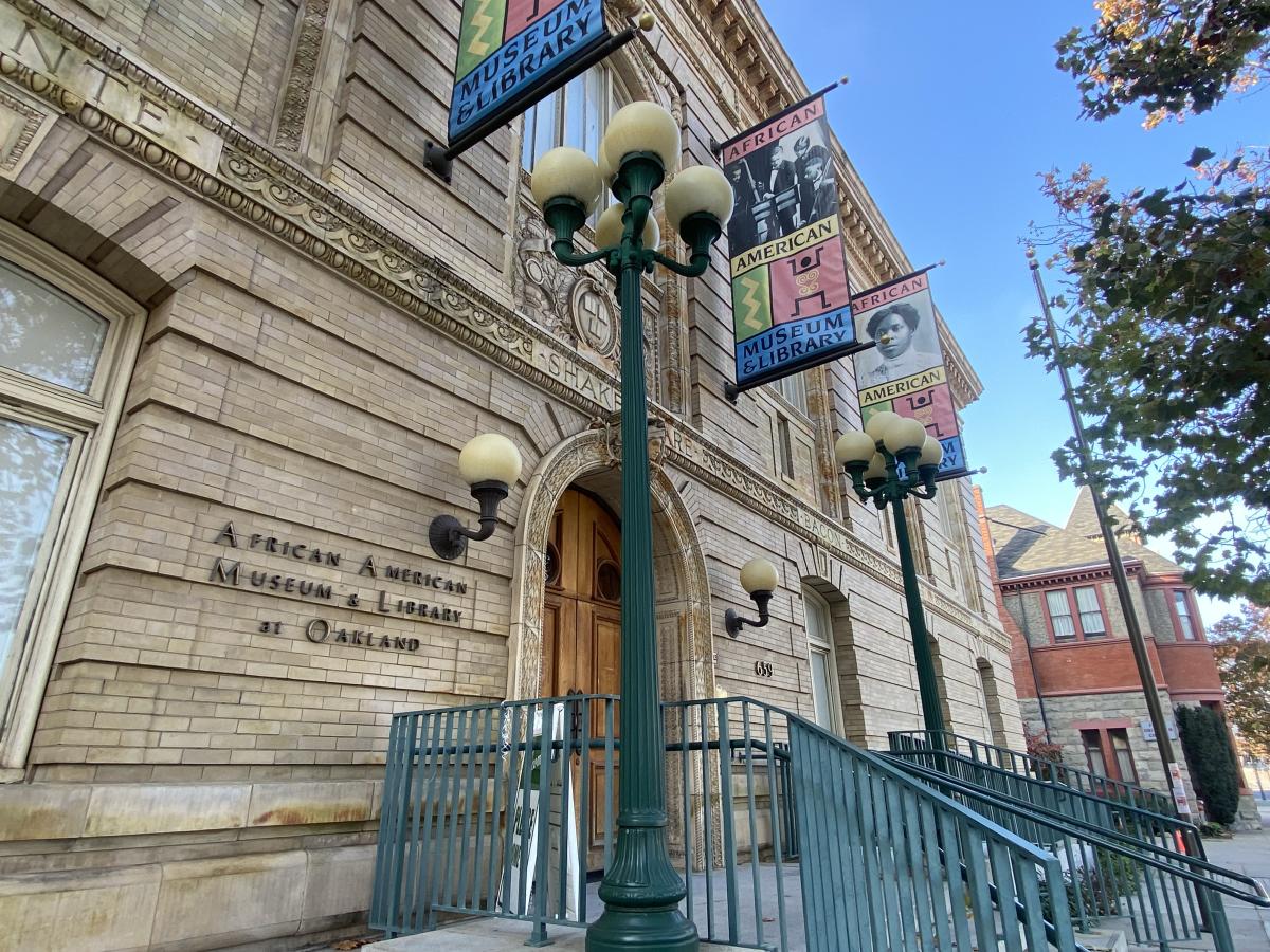 A pale brick building with green rails adorned with colorful flags depicting prominent figures in African American history