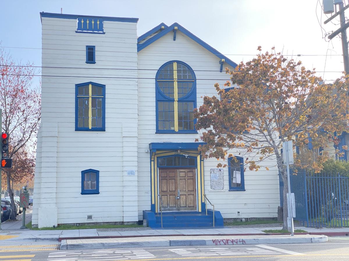 A cream colored church with blue trim surrounded by fall trees