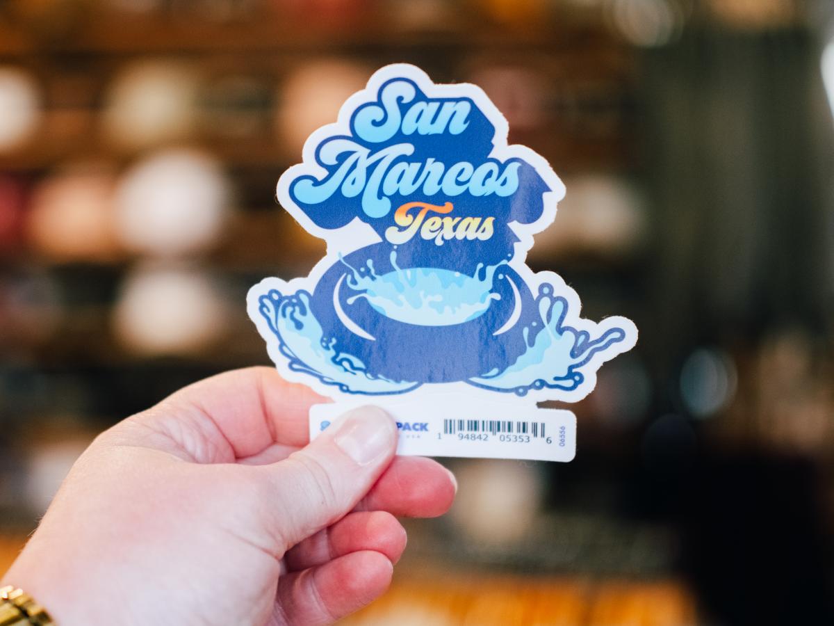 A San Marcos sticker held up at Barefoot in Downtown San Marcos, Texas