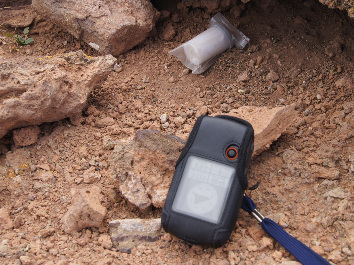 gps next to a geocache container in rocks and sand