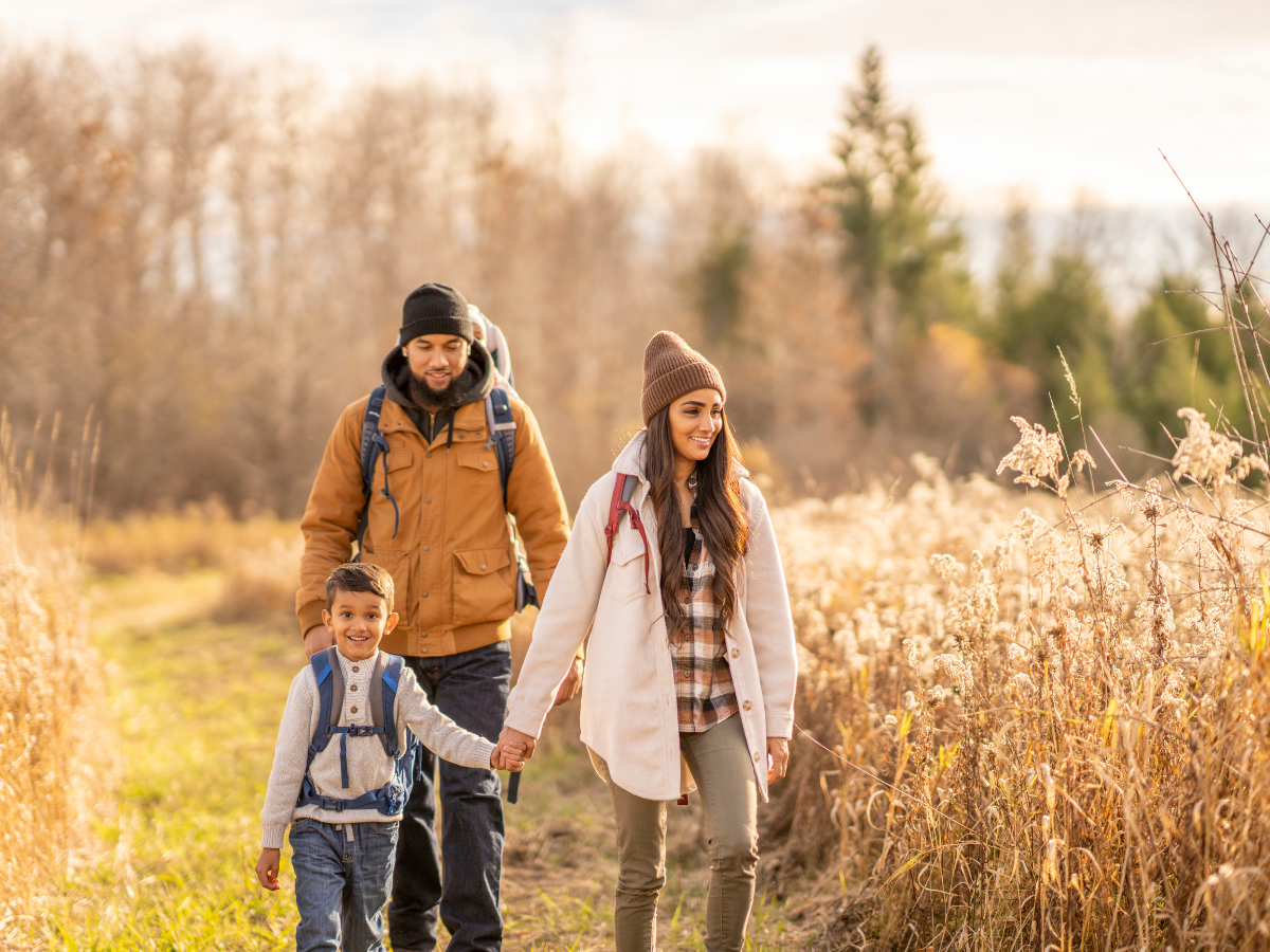 A family happily hiking through a trail with the changing autumn trees behind them in Seneca County, NY.