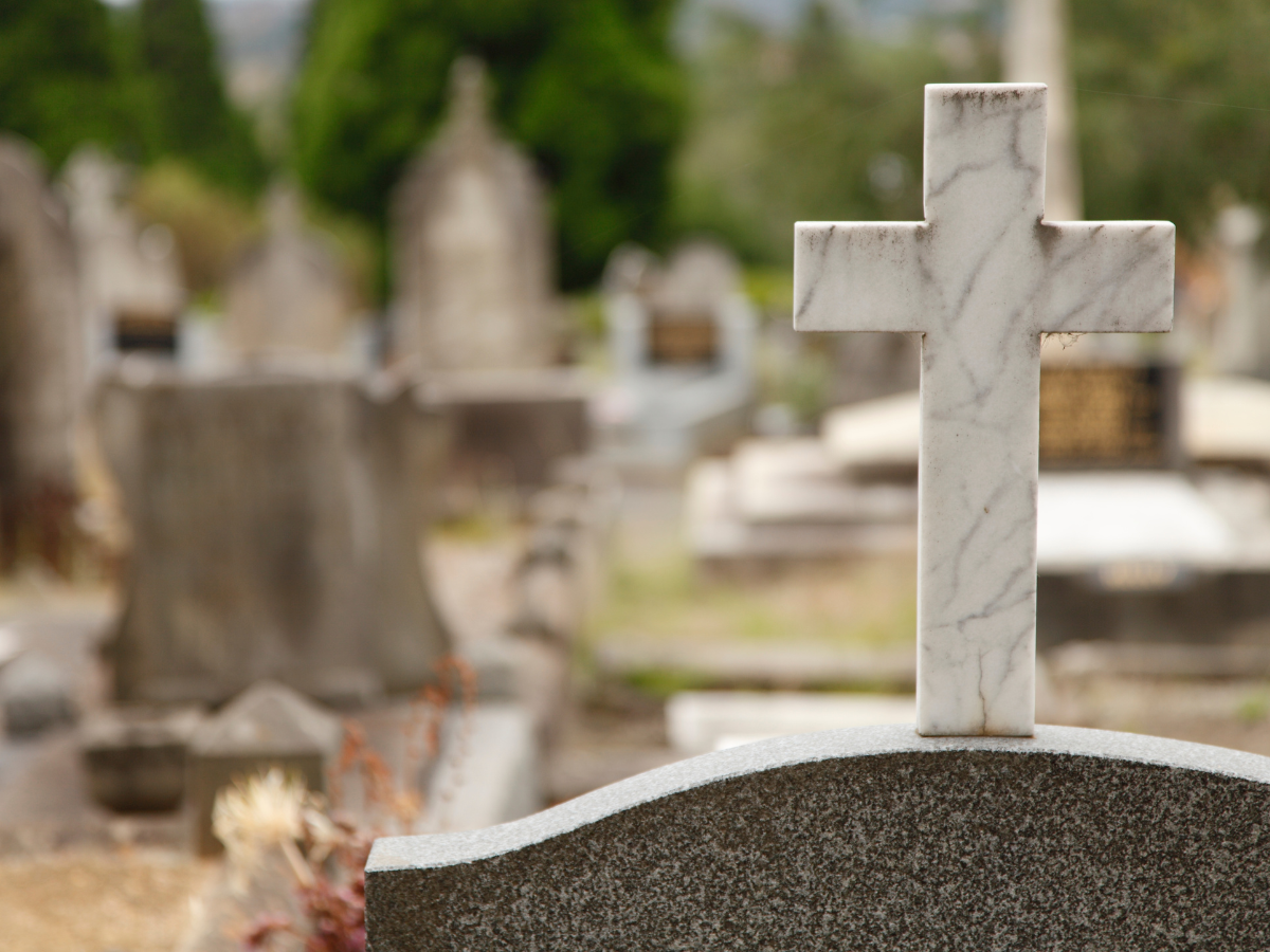 close up of a headstone with a marble cross on top in a cemetery