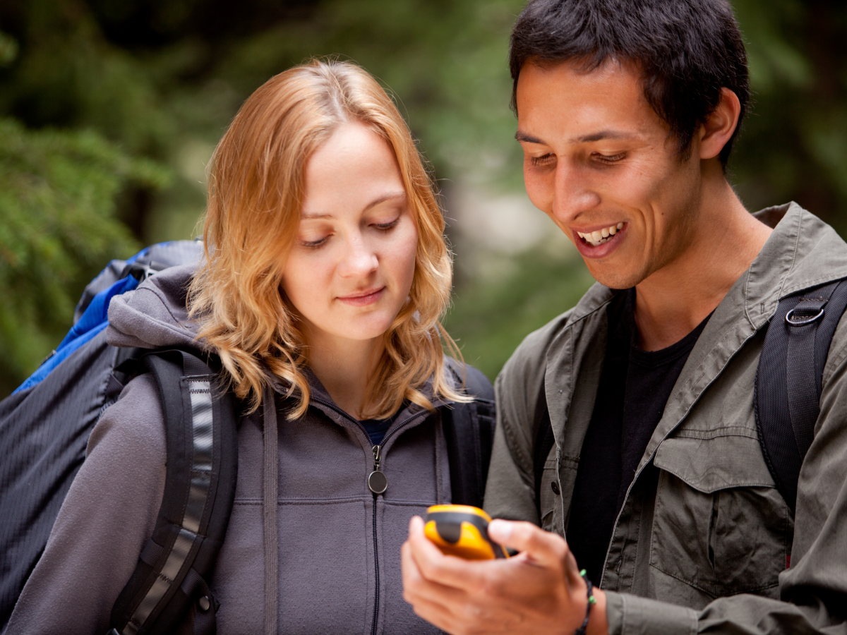 two people looking at a yellow gps between them on a hike