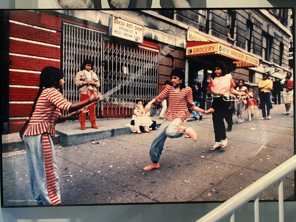 photograph of women playing with a jump rope on a busy sidewalk wearing matching red and white striped outfits