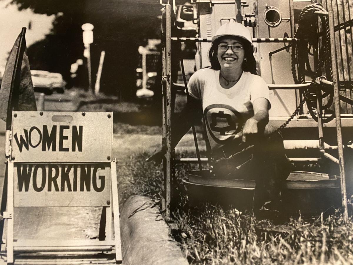 Woman wearing a white hard hat sitting near a train with a sign that says Women Working
