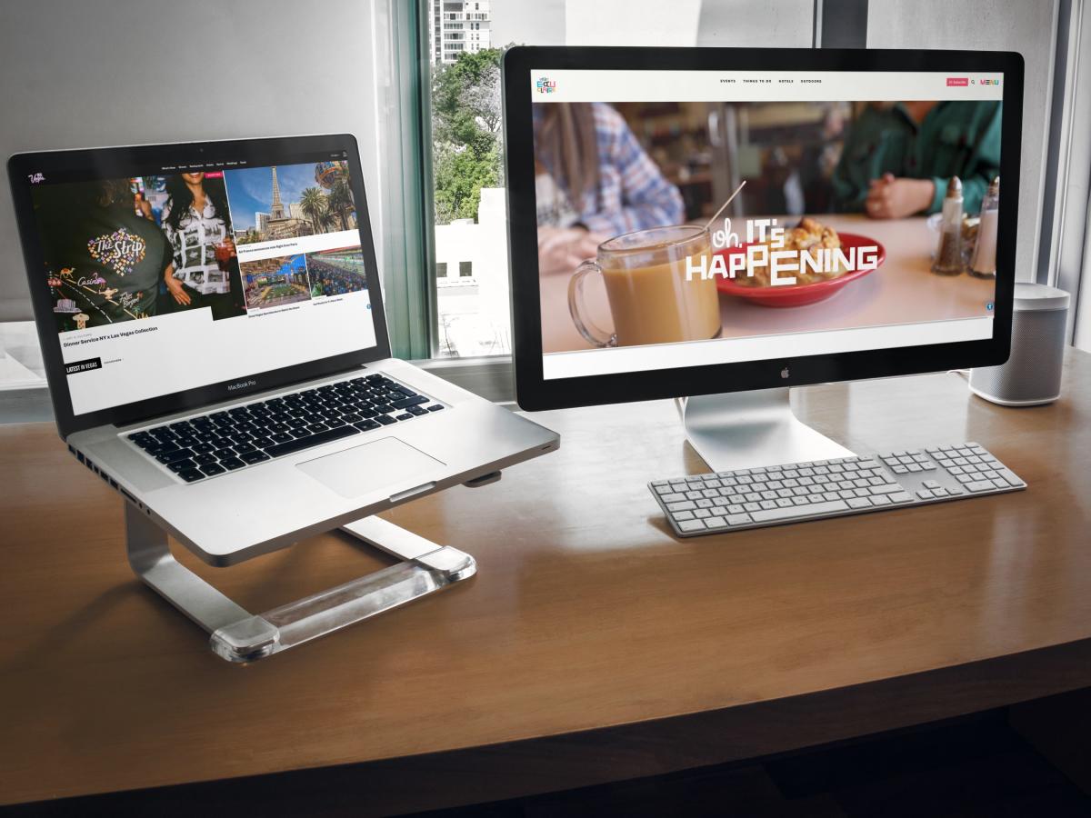 The Visit Las Vegas website homepage opened up on a laptop next to a desktop monitor featuring the Visit Eau Claire website.