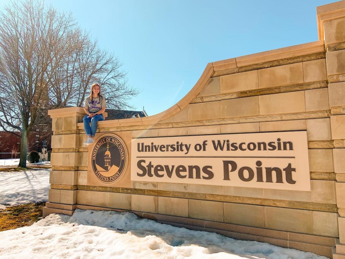 Girl sitting on the University of Wisconsin Stevens Point Sign.