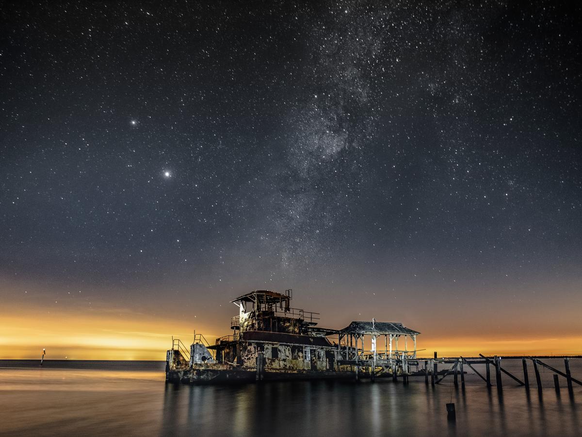 An old barge anchored on Lake Pontchartrain under a starry sky at dusk.