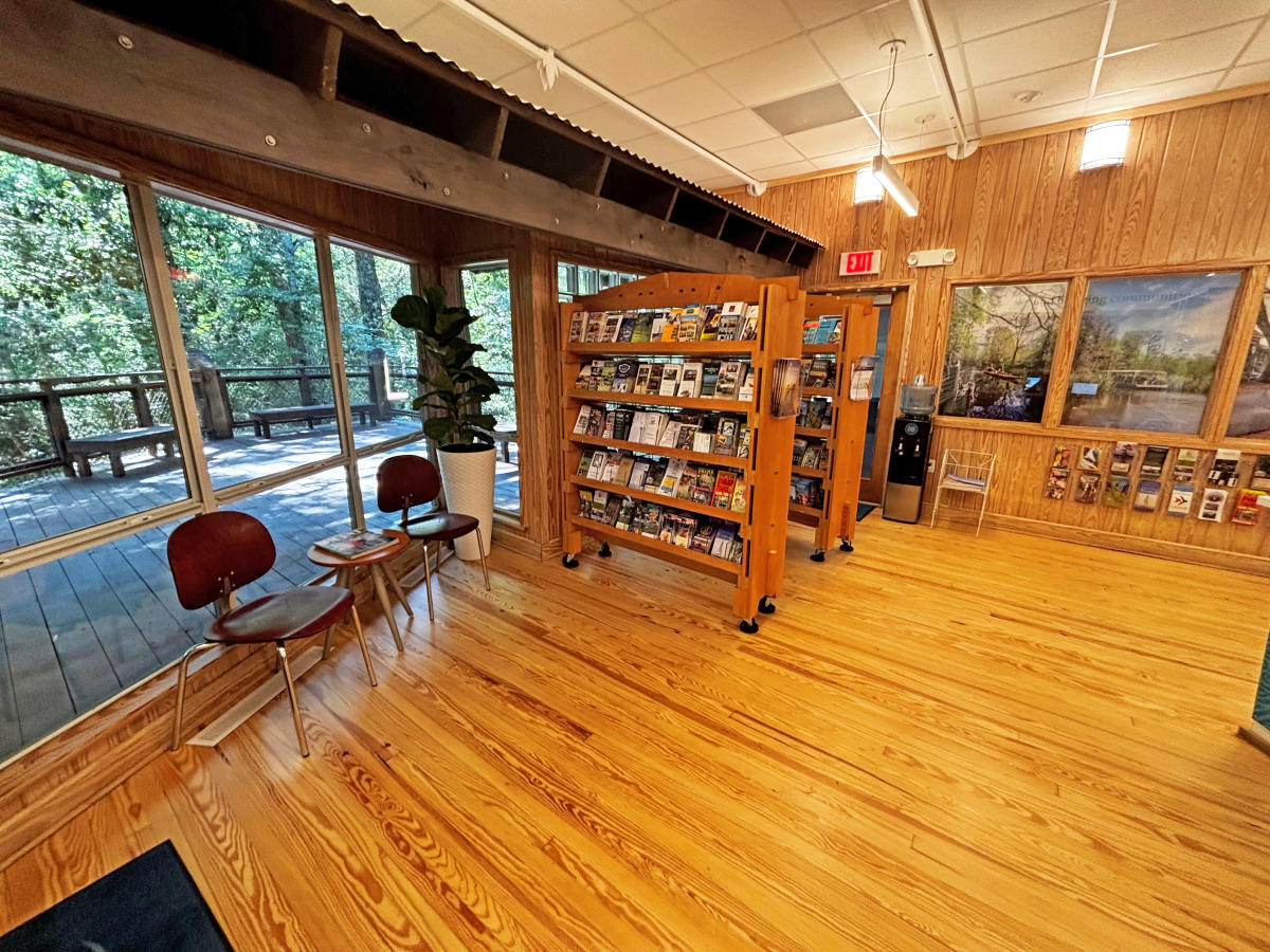 Brochure shelves featuring local and statewide attractions fill the lobby of the Visit The Northshore Visitor Center beside large windows overlooking the wooded deck.
