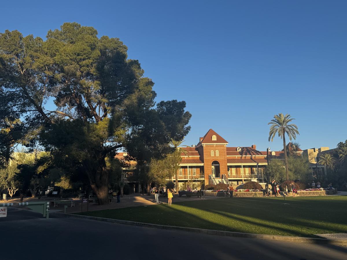 Old Main at the University of Arizona surrounded by trees and people in the late afternoon sun.