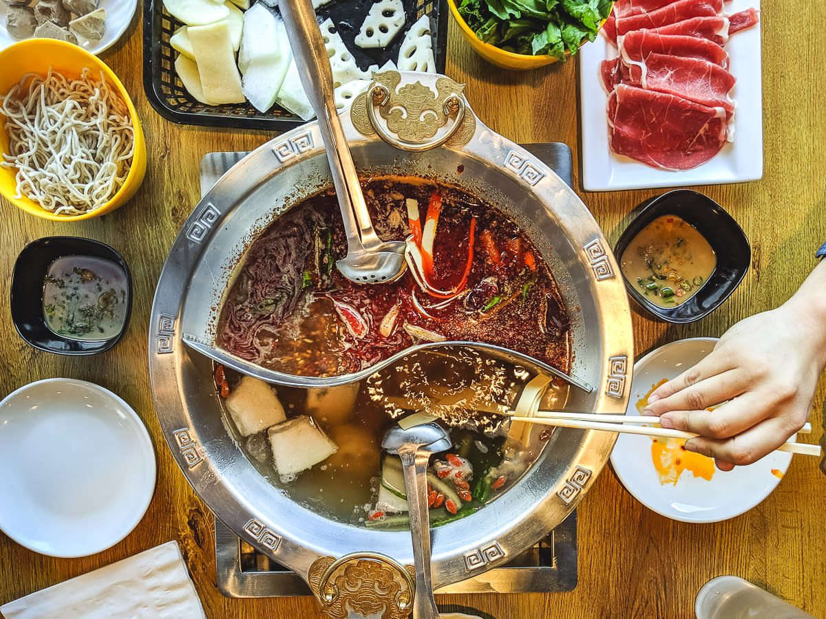 Hot Pot bowl with several spoons and food surrounding the pot