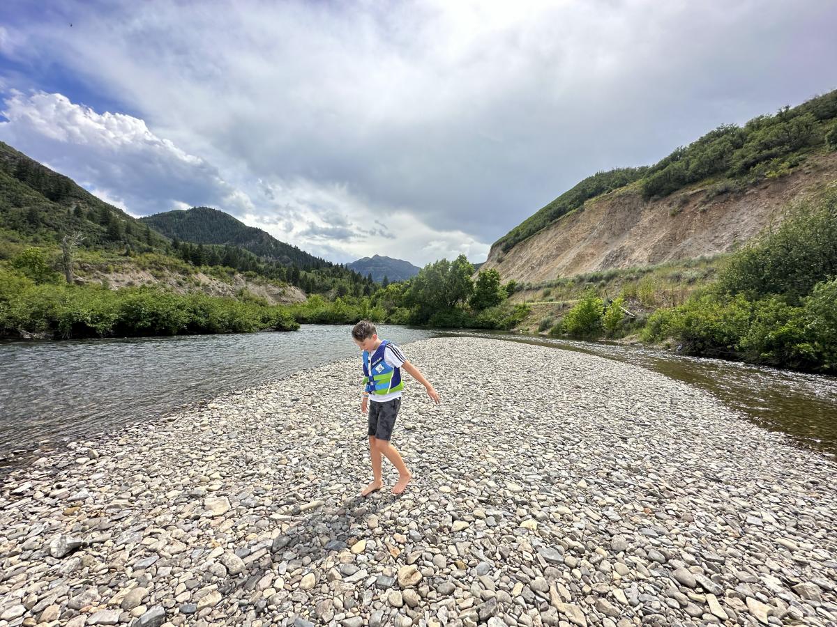 Boy playing on the rocky beach by the Provo River