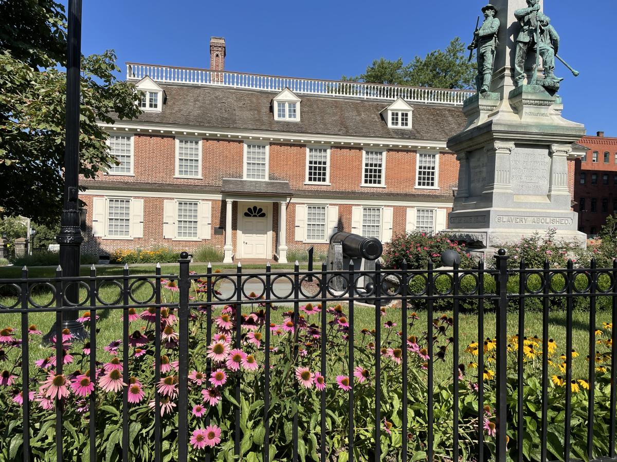 The exterior of Philipse Manor Hall with purple and yellow flowers blooming in the foreground.