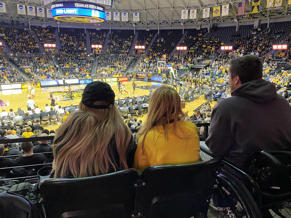 A young man in a wheelchair enjoys a Wichita State Shockers Basketball game at Charles Koch Arena with two female companions